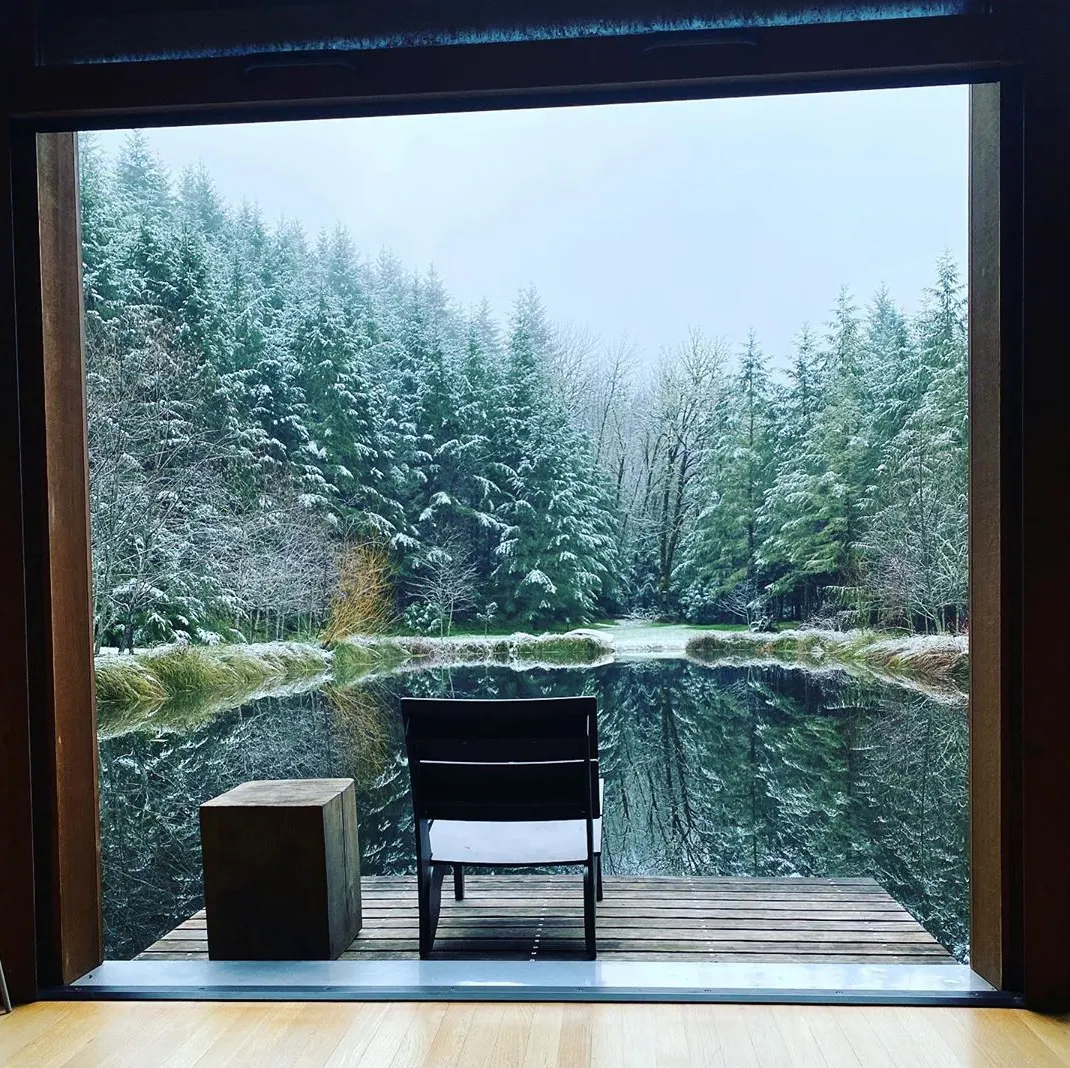 Peaceful view of a chair and table on a small dock overlooking a winter forest